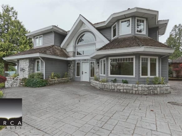 Elegant grey craftsman-style house with stone accents, large front windows, and a spacious paved driveway, showcasing prime real estate opportunity with Orca Realty Inc.