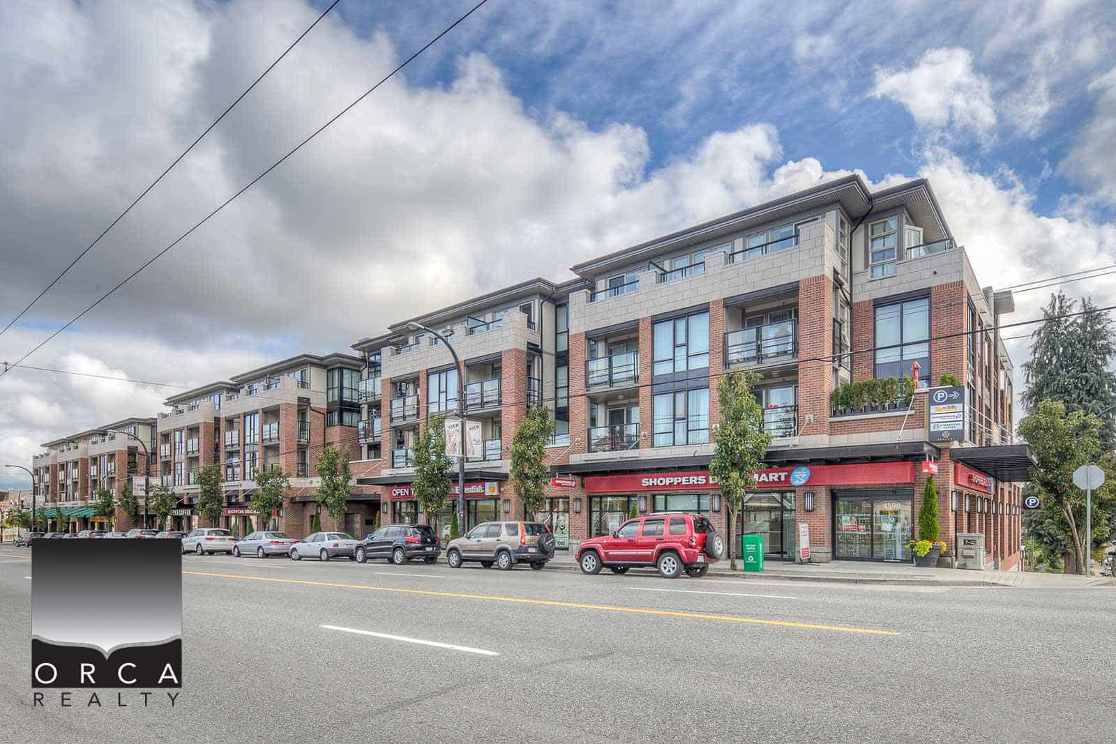 Modern mixed-use apartment building with retail stores on the ground floor, located in a busy urban area with parking and storefronts.