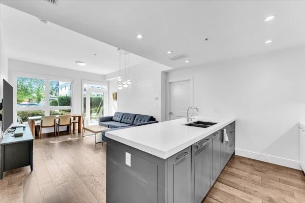 Spacious and bright interior of a Vancouver condo at 101-7878 Granville Street, showcasing an open-concept living area with large windows, a sleek kitchen, and contemporary furnishings.
