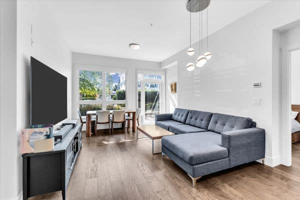 Bright and spacious living room in a Vancouver condo at 101-7878 Granville Street, featuring a large gray sectional sofa, hardwood floors, and ample natural light.