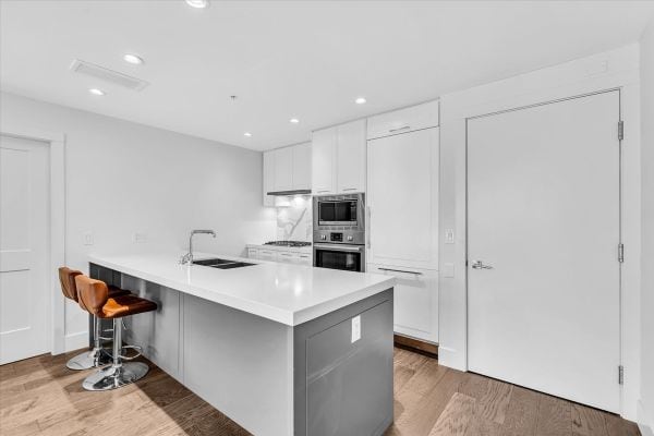 Spacious kitchen at 101-7878 Granville Street, Vancouver, featuring sleek white cabinets, a large island, and modern appliances, perfect for contemporary urban living.