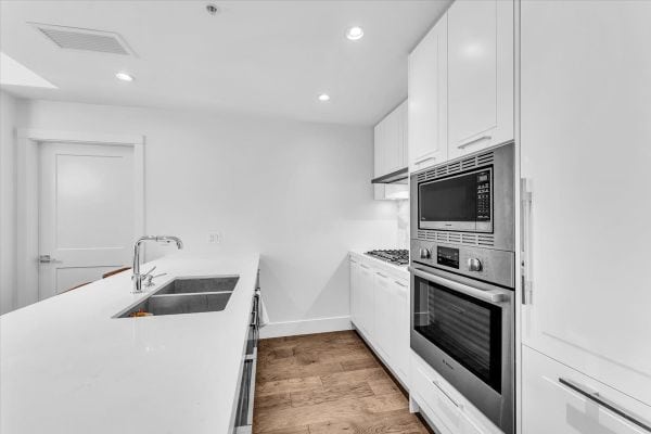Spacious kitchen in Vancouver featuring sleek white cabinets, built-in microwave and oven, and a contemporary design perfect for modern living.
