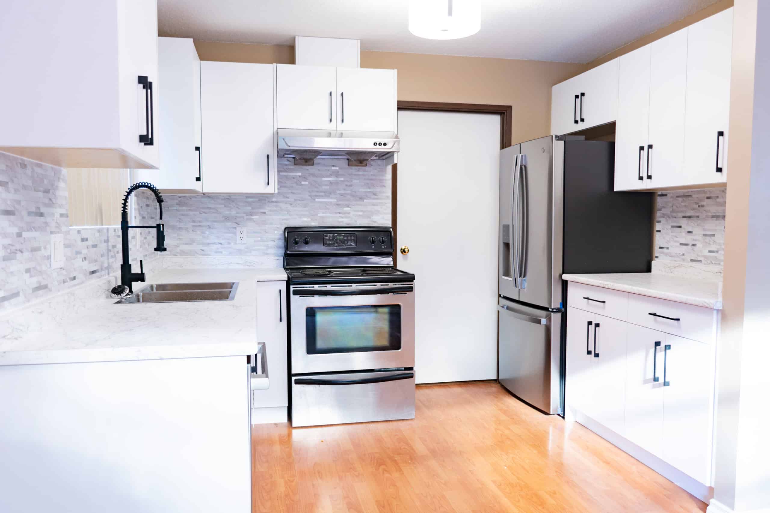 Modern kitchen with stainless steel appliances and white cabinetry Modern kitchen with stainless steel appliances, white cabinets, and a light grey backsplash, located at 1951 Coquitlam Avenue, Port Coquitlam, ideal for comfortable living.