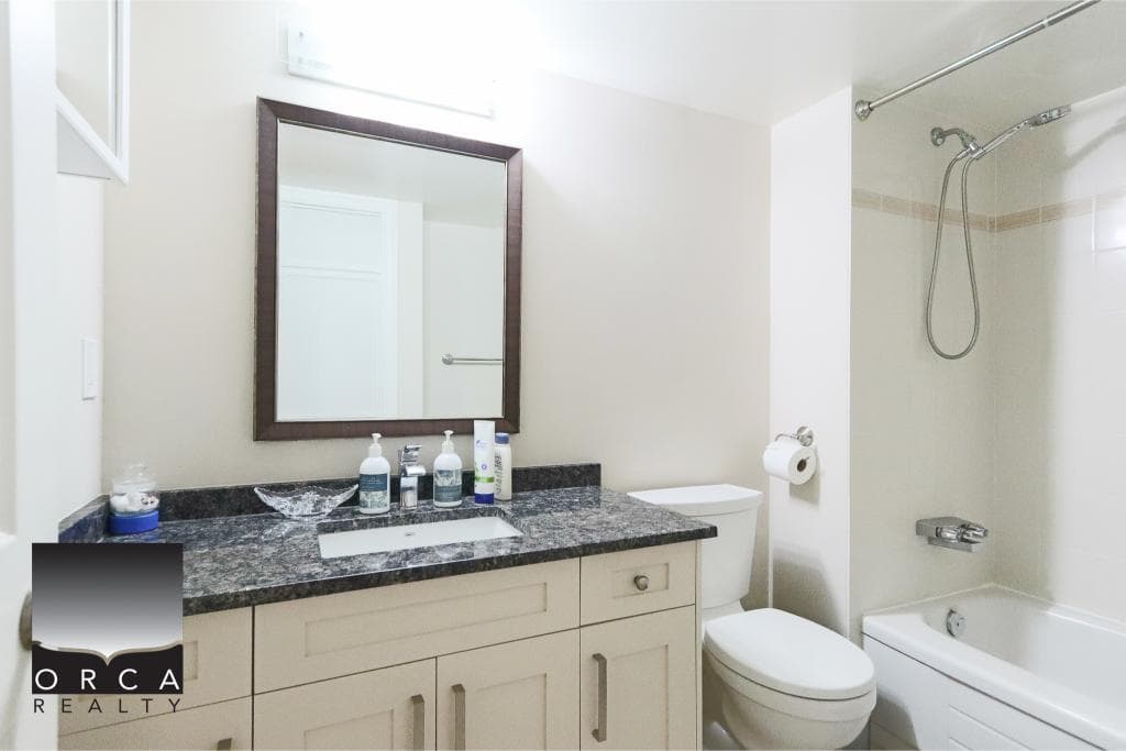 Modern bathroom with white vanity, granite countertop, mirror, toilet, and bathtub with shower; ideal for Vancouver real estate listings.