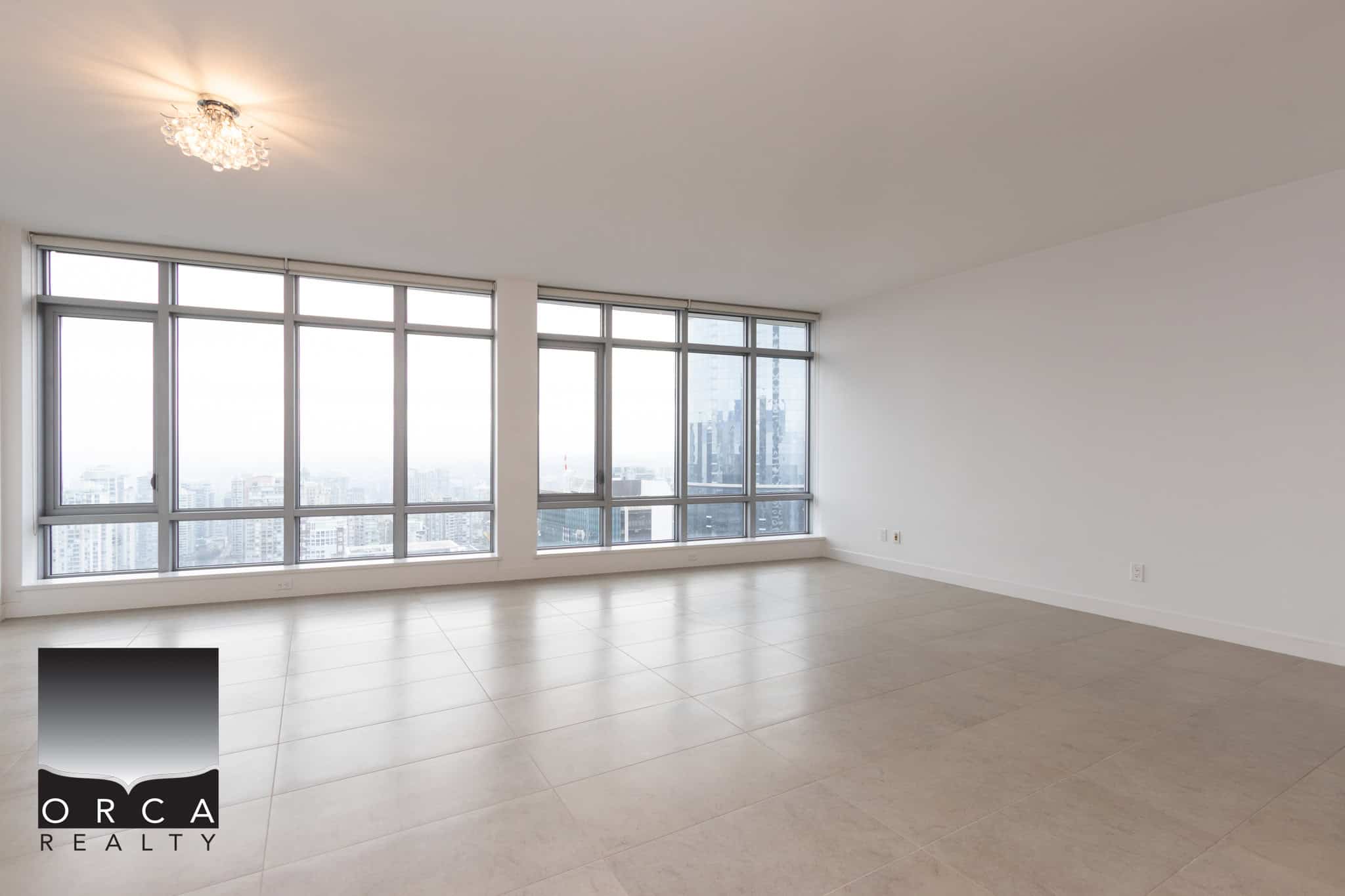 Panoramic view of modern high-rise condo living room with large floor-to-ceiling windows, natural daylight, neutral tile flooring, and minimalist white walls; ideal for urban real estate in Vancouver.
