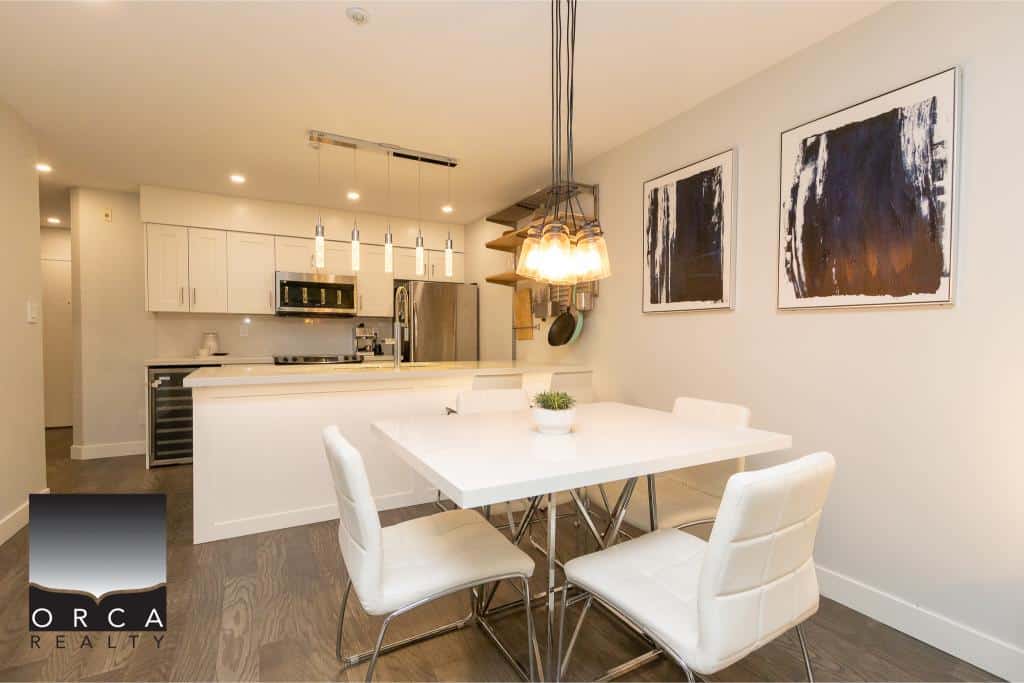 Modern open-concept kitchen and dining area with stylish white cabinetry, sleek appliances, and contemporary artwork, perfect for Vancouver-area homebuyers.