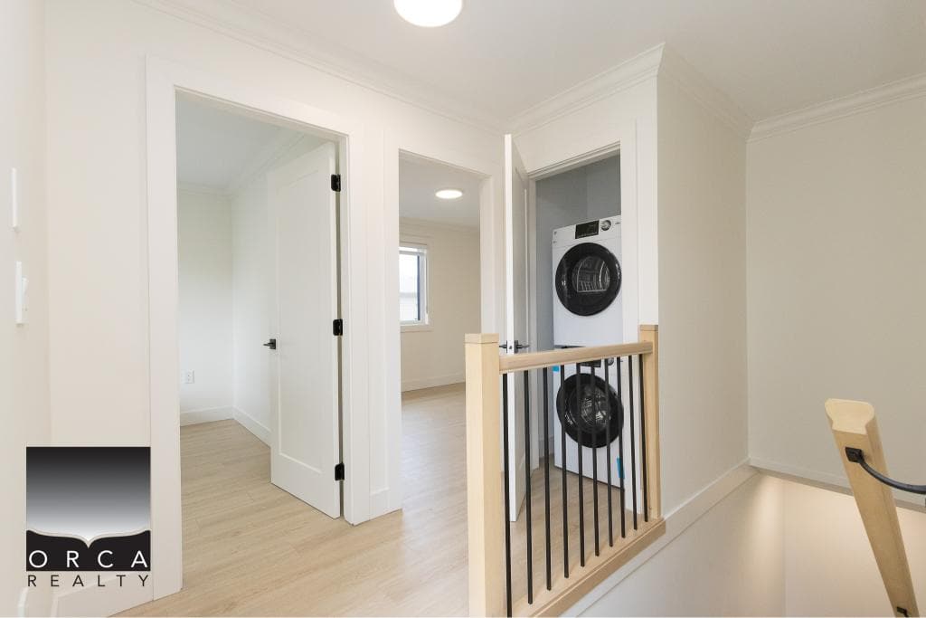 Bright laundry area in modern home with washer and dryer, white interior, hardwood floors, and natural light from window, showcasing Vancouver Island real estate.