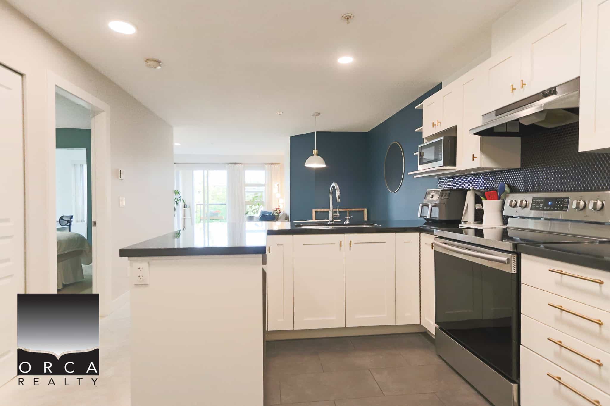 Modern kitchen with white cabinetry, black countertops, stainless steel appliances, and a blue accent wall, showcasing Vancouver real estate options from Orca Realty Inc.