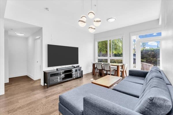 Spacious living room at 101-7878 Granville Street, Vancouver, featuring a comfortable gray sofa, large windows with natural light, and contemporary decor, ideal for relaxing or entertaining.