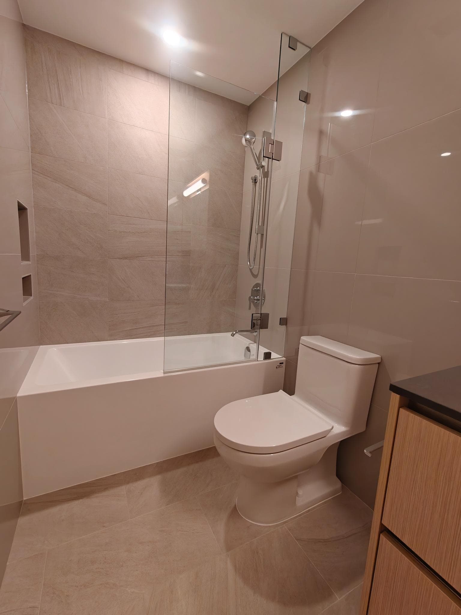 Modern bathroom with bathtub, walk-in shower, and beige tile decor, featuring a sleek toilet and wooden vanity, perfect for Vancouver Island homes.