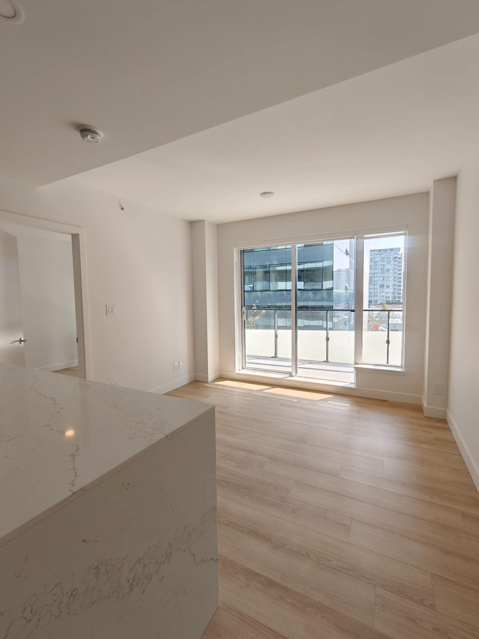 Bright modern apartment interior with large glass sliding doors, white walls, and light wood flooring, showcasing contemporary condo living in Vancouver.