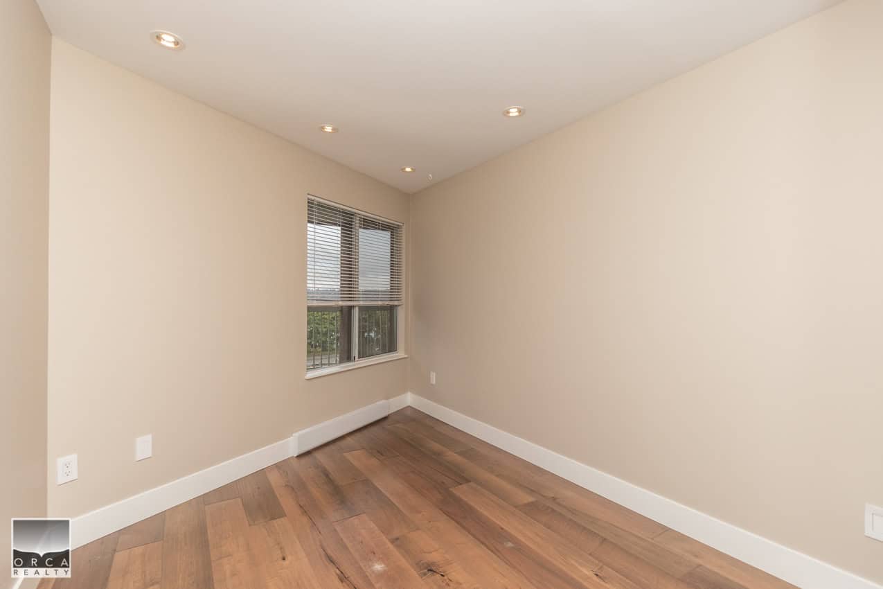 Bright empty room with hardwood flooring, beige walls, and a large window with blinds, ideal for a modern home interior, listed by Orca Realty Inc.