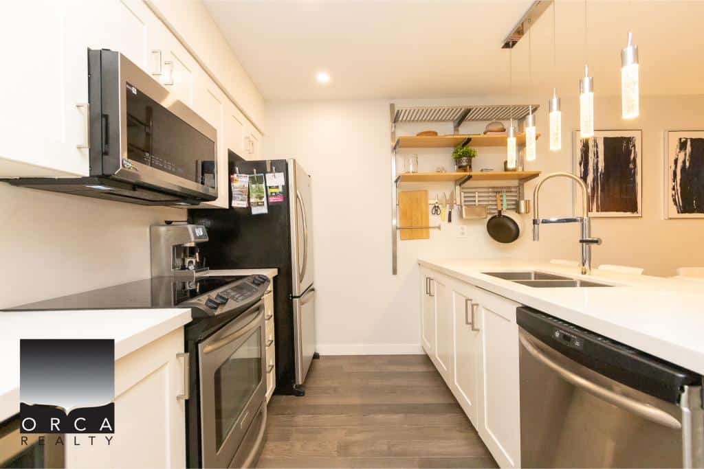 Modern kitchen with stainless steel appliances, white cabinetry, and open shelving, perfect for Vancouver real estate buyers seeking stylish and functional homes.