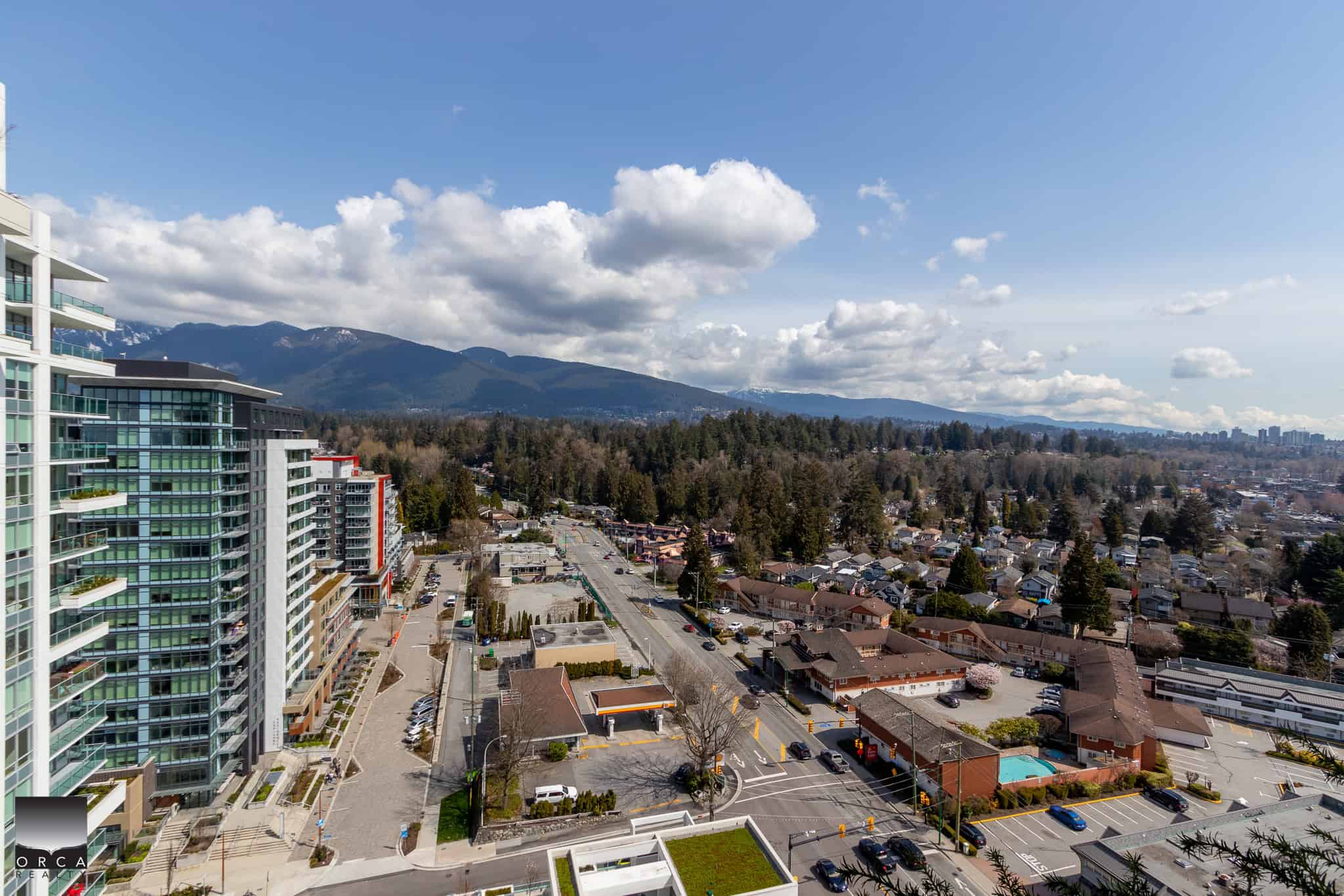 Panoramic view of Vancouver's cityscape with modern high-rise condos and surrounding residential neighborhood, showcasing mountain backdrop and blue sky, ideal for real estate marketing in Vancouver.