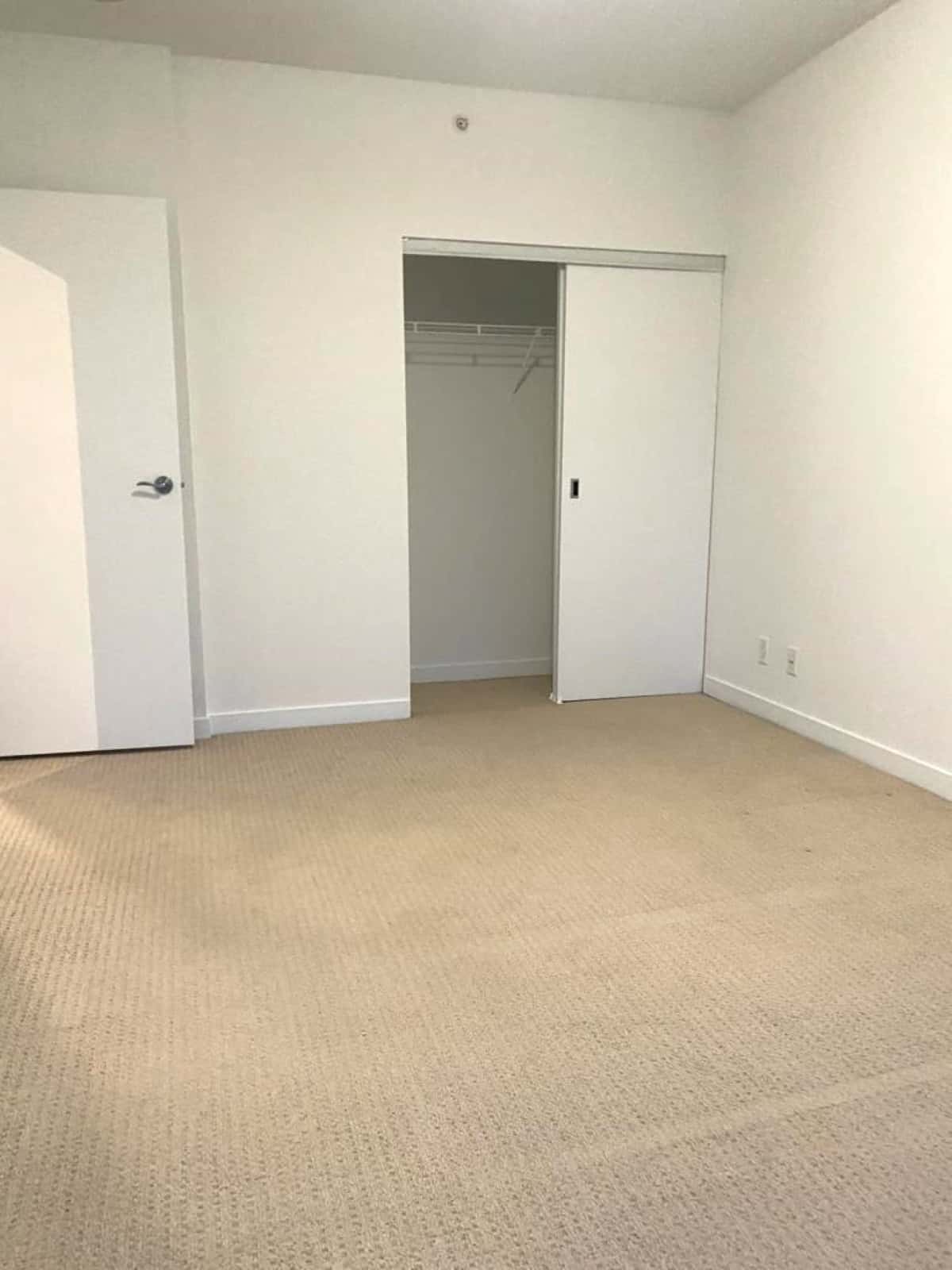 Bright empty bedroom with beige carpet, white walls, built-in closet, and modern door, ideal for Vancouver property listings and real estate services by Orca Realty Inc.