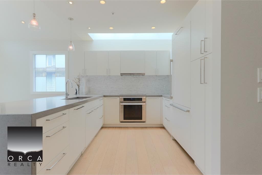 Modern white kitchen with stainless steel appliances, ample cabinetry, and natural light - perfect for Vancouver Island homes.