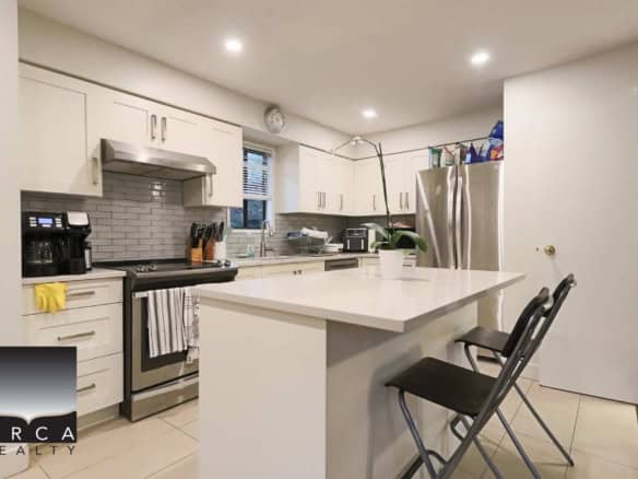 Bright modern kitchen featuring white cabinetry, stainless steel appliances, a central island with a white countertop, and a tiled backsplash, perfect for family living and entertaining.