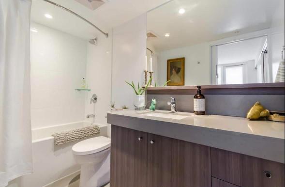 Modern bathroom with white tub, shower, and vanity featuring a large mirror, decorated with minimal accessories, situated in a contemporary home listed by Orca Realty Inc.