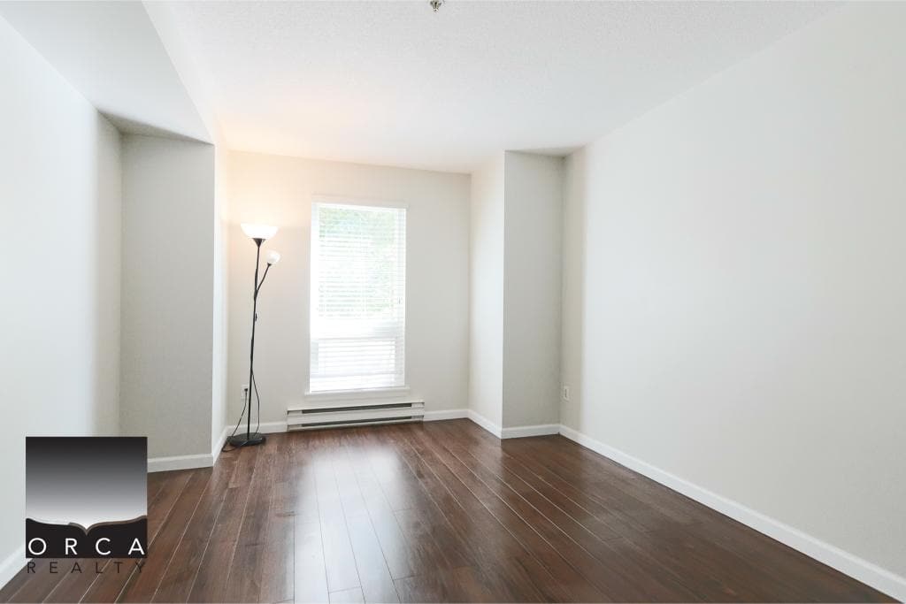 Bright empty rental condo room with large window and hardwood flooring - Orca Realty Inc.