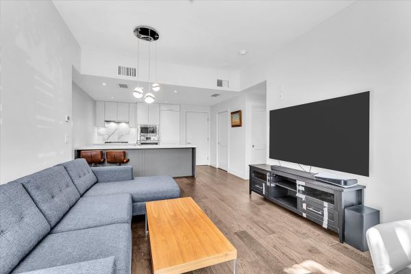 Bright and spacious living room in a Vancouver condo at 101-7878 Granville Street, featuring a comfortable gray sectional sofa, large flat-screen TV, and contemporary decor.