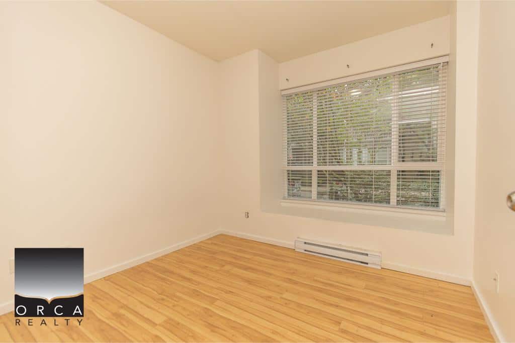 Bright empty room with hardwood floors and large window, ideal for Vancouver real estate buyers, showcasing a clean and modern interior.