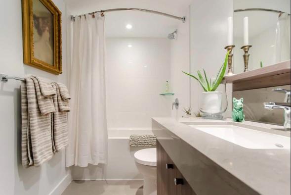 Spacious modern bathroom with white fixtures and elegant decor, featuring a bathtub, vanity with potted plant, and decorative candles, showcasing quality home amenities.