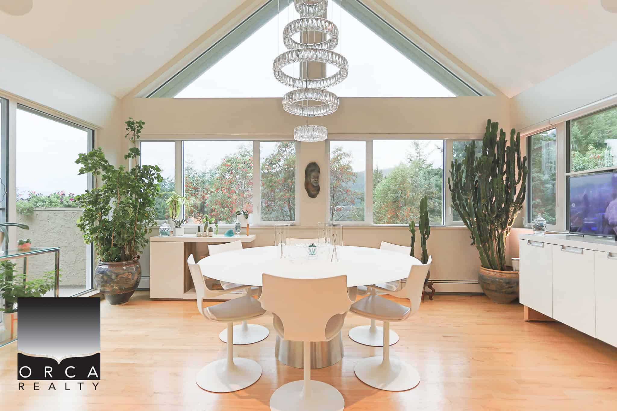 Luxurious modern dining room with expansive windows, natural light, and indoor plants, showcasing upscale real estate listings by Orca Realty Inc. in Canada.