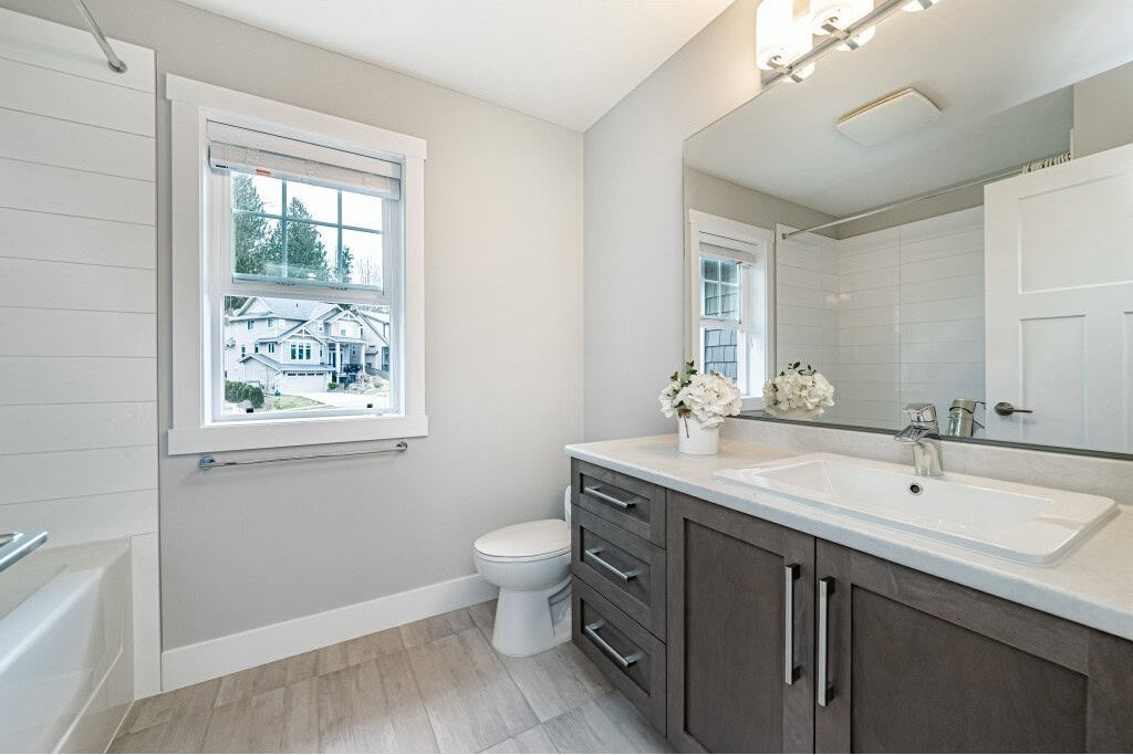 Bright modern bathroom with white and grey decor, spacious vanity with storage, large mirror, and natural light, perfect for homes listed by Orca Realty Inc.
