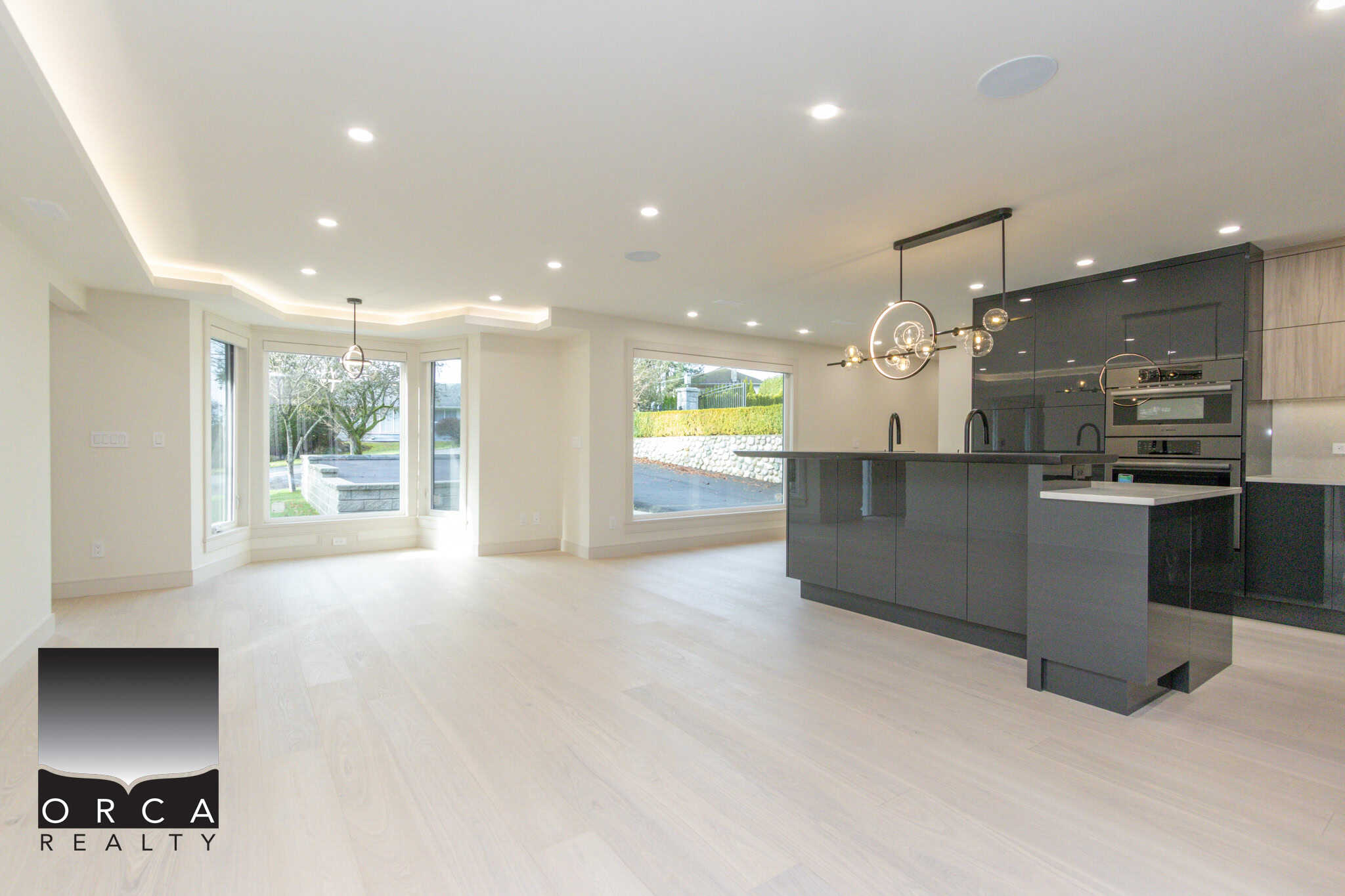 Bright modern open-concept kitchen and living space with large windows, sleek black cabinetry, stylish pendant lighting, and natural light—perfect for Vancouver Island real estate buyers.