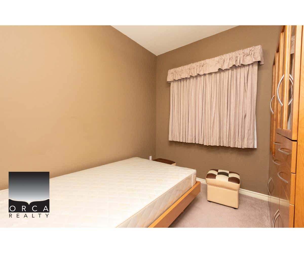Comfortable bedroom with beige walls and a window with cream curtains, featuring a wooden bed frame and matching wardrobe, ideal for home buyers and real estate listings in Ontario.