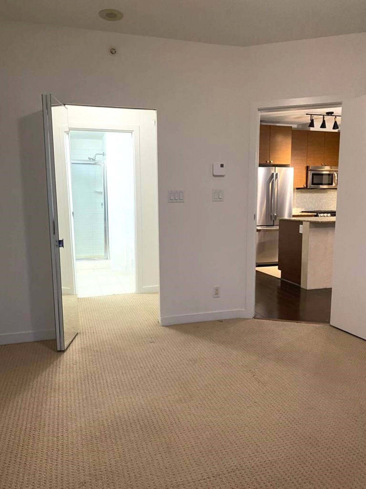 Bright empty living room with beige carpet, leading to modern kitchen and bathroom, showcasing Vancouver property listings and real estate services by Orca Realty Inc.