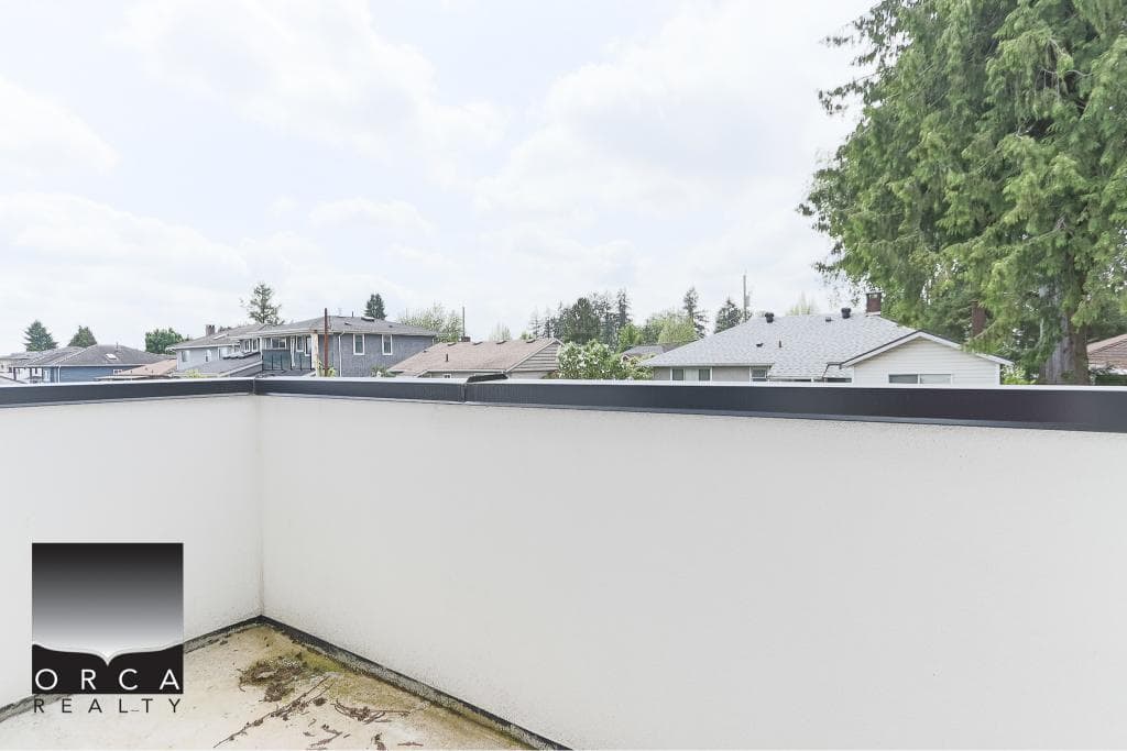 Spacious balcony with modern white walls and black trim, overlooking a neighborhood with trees and residential homes, perfect for enjoying outdoor living in Vancouver.