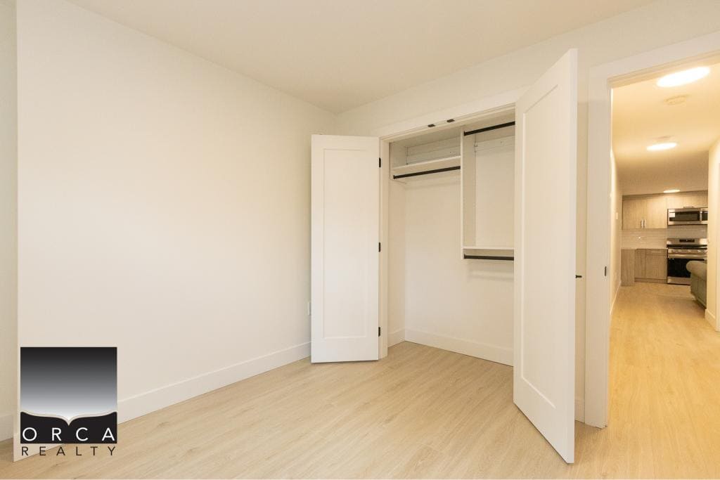 Bright modern bedroom with ample closet space, white walls, and light wood flooring, showcasing Orca Realty Inc.'s luxury real estate offerings in Vancouver.