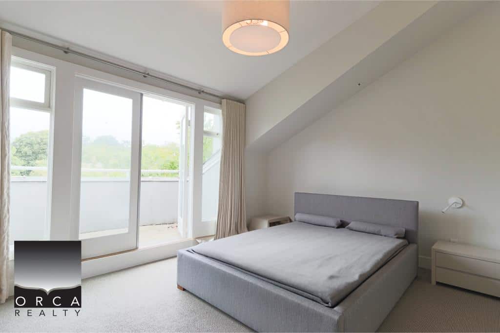 Bright modern bedroom with large balcony doors, minimalist decor, and natural light, ideal for Vancouver Island real estate buyers seeking stylish homes | Orca Realty Inc.