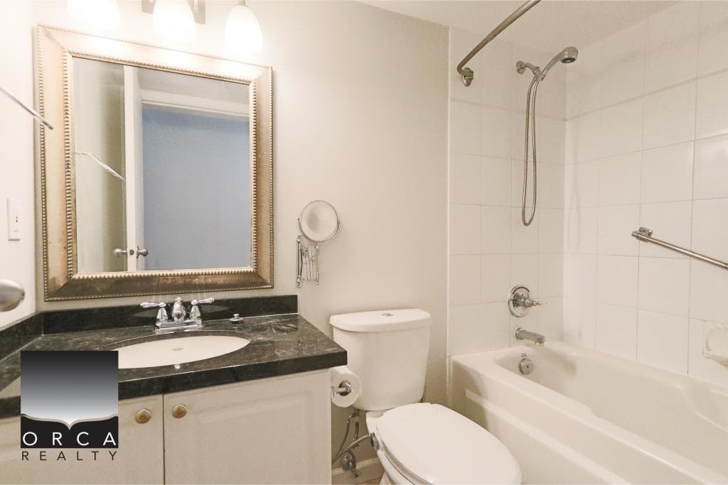 Bright bathroom featuring a modern vanity with a black countertop, a large framed mirror, and a combination bathtub and shower with white tiles, ideal for comfortable home living.