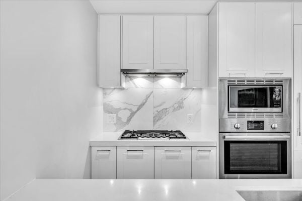 Modern white kitchen featuring built-in microwave and oven, sleek cabinetry, and marble backsplash, ideal for Vancouver homebuyers seeking contemporary kitchen designs.