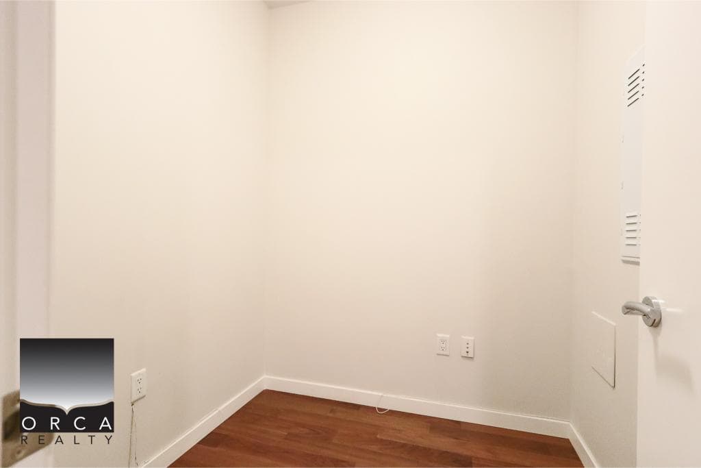 Empty small room with white walls, electrical outlets, and a wood floor, suitable for office or storage in a residential property listed by Orca Realty Inc.