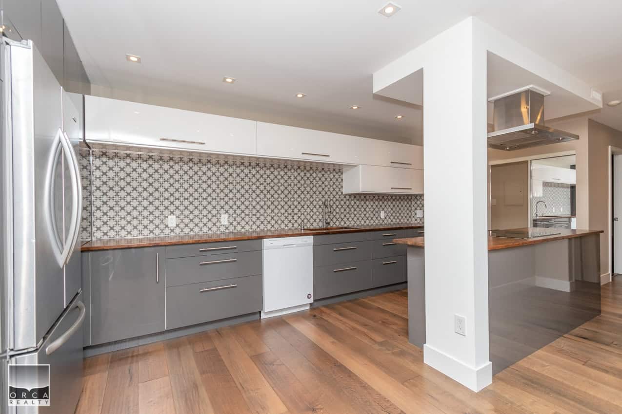 Modern kitchen with grey cabinetry, stainless steel appliances, patterned backsplash, and hardwood floors, perfect for contemporary home living.