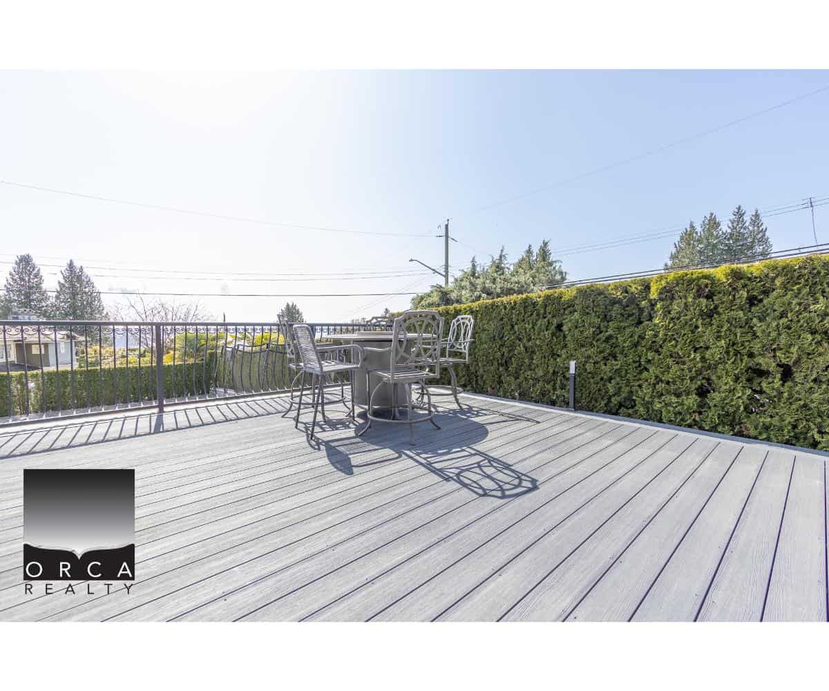 Spacious outdoor deck with seating area, perfect for relaxing or entertaining in Vancouver's real estate market. Features a modern railing and lush privacy hedge.