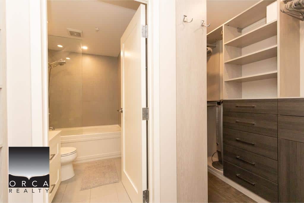 Bright modern bathroom with walk-in shower and ample storage, connected to walk-in closet with built-in shelves and drawers, showcasing sleek design for Vancouver real estate.