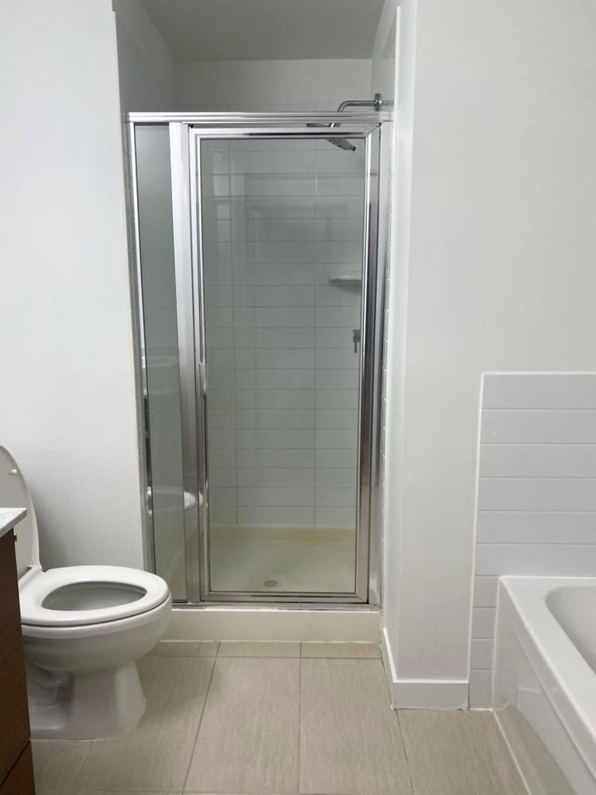 Bright bathroom shower stall with glass door, modern fixtures, white tiles, and beige flooring, showcasing a clean and functional space inside a residential property listed by Orca Realty Inc.