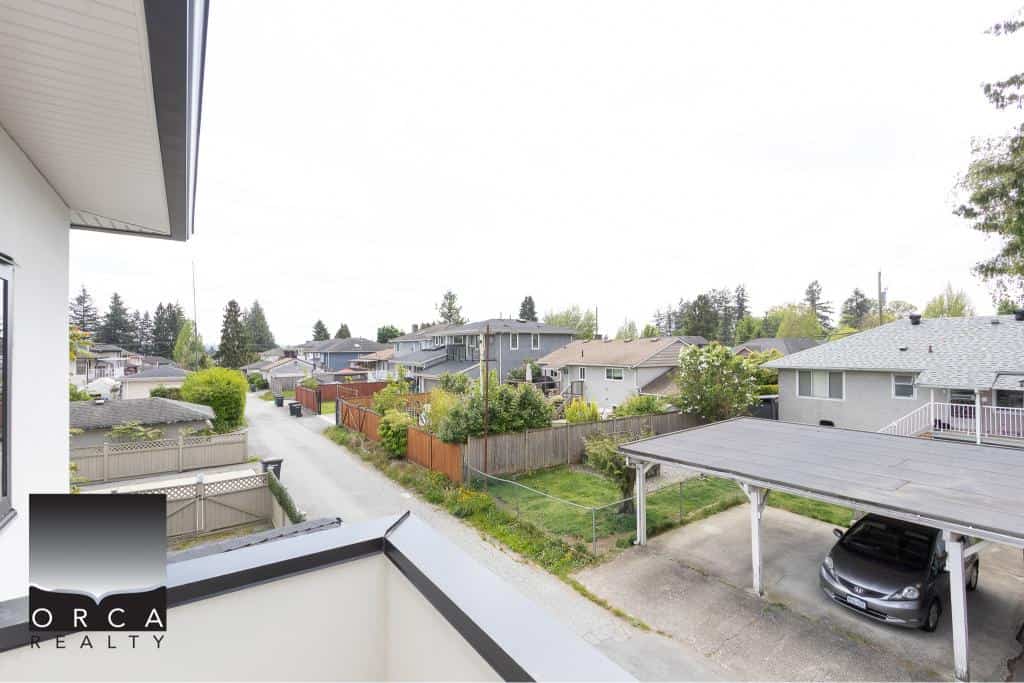 Bright residential neighbourhood view from balcony, showcasing suburban homes, greenery, and parking spaces in a Vancouver area. Ideal for real estate and property investment branding.