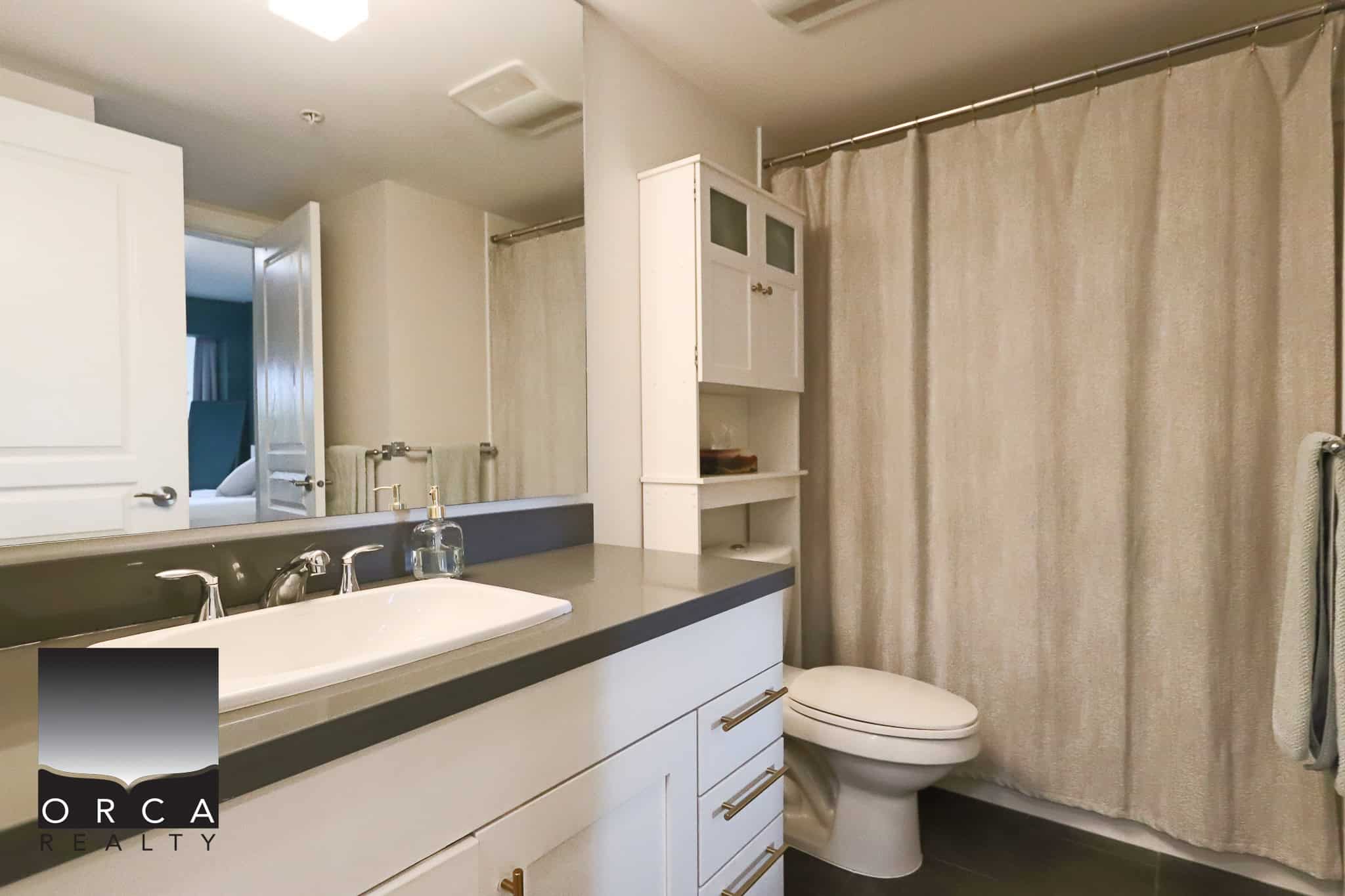 Modern bathroom with white cabinetry, black countertop, and beige shower curtain, featuring a sleek sink and fixtures, perfect for Vancouver island living.