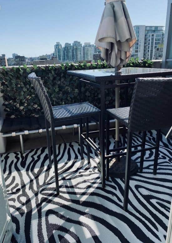 Balcony outdoor seating area with a zebra print rug, black metal table, chairs, and city skyline view in the background, ideal for urban living and real estate in Vancouver.