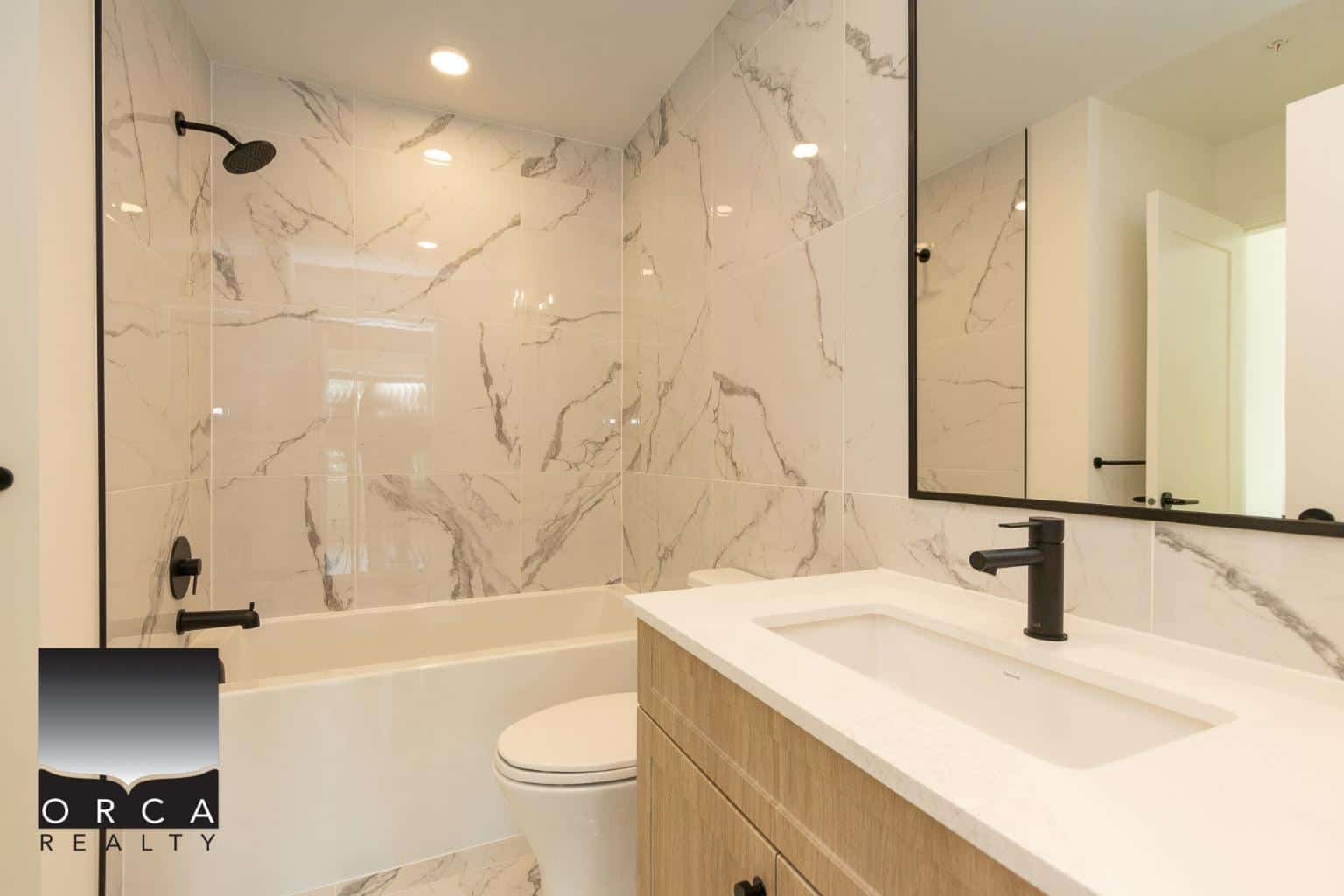 Modern bathroom with marble tile walls, black fixtures, vanity with integrated sink, and large mirror, showcasing contemporary interior design and luxury home features.