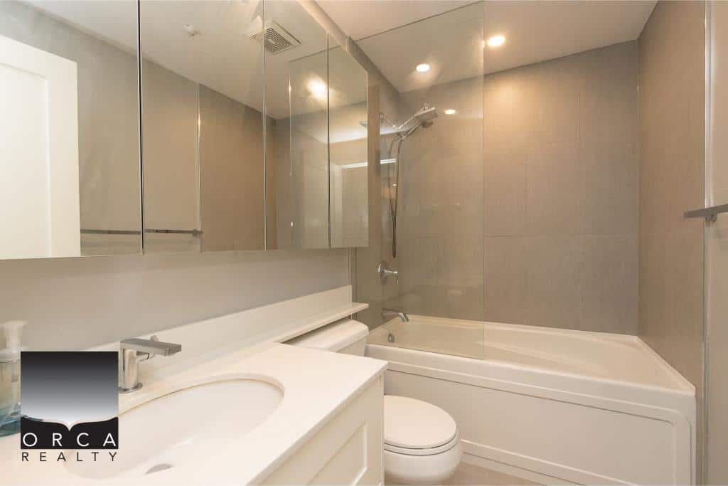 Modern bathroom with neutral tones, glass shower enclosure, and sleek fixtures, showcasing upscale interior design by Orca Realty Inc. for Vancouver Island homes.
