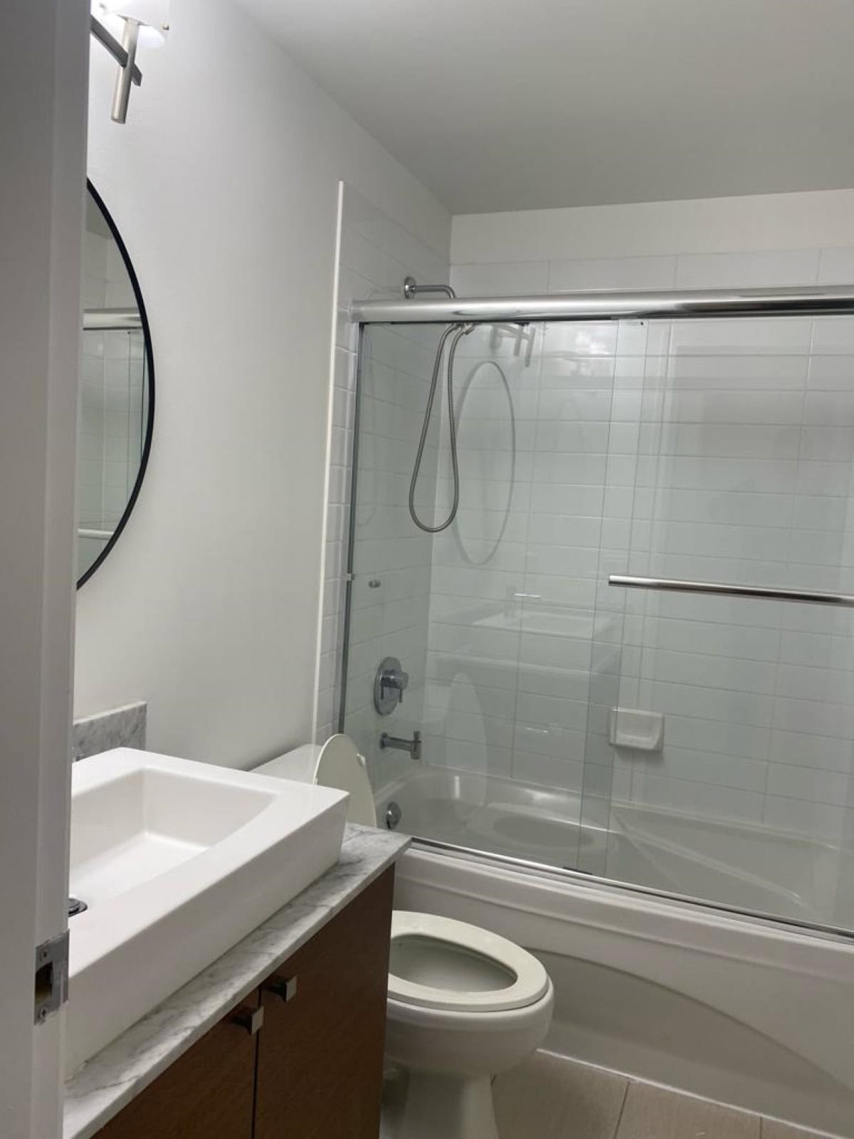 Modern bathroom with walk-in shower, white tiled walls, sleek vanity with marble countertop, round mirror, and contemporary fixtures, perfect for Ontario real estate listings by Orca Realty Inc.