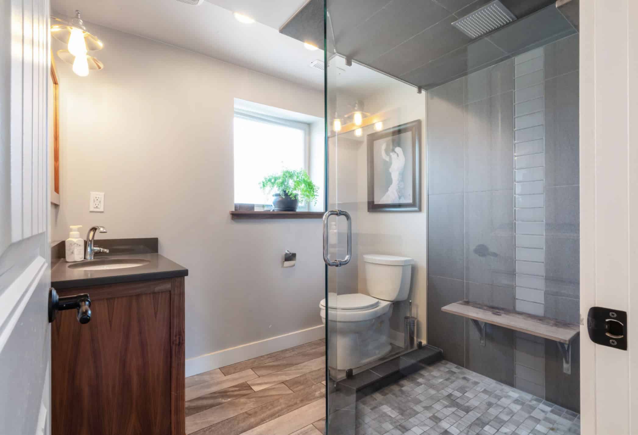 Screenshot Bright modern bathroom with glass shower, wooden accents, and natural light, featuring contemporary fixtures, stylish tile work, and a cozy window seat for a luxurious home feel.