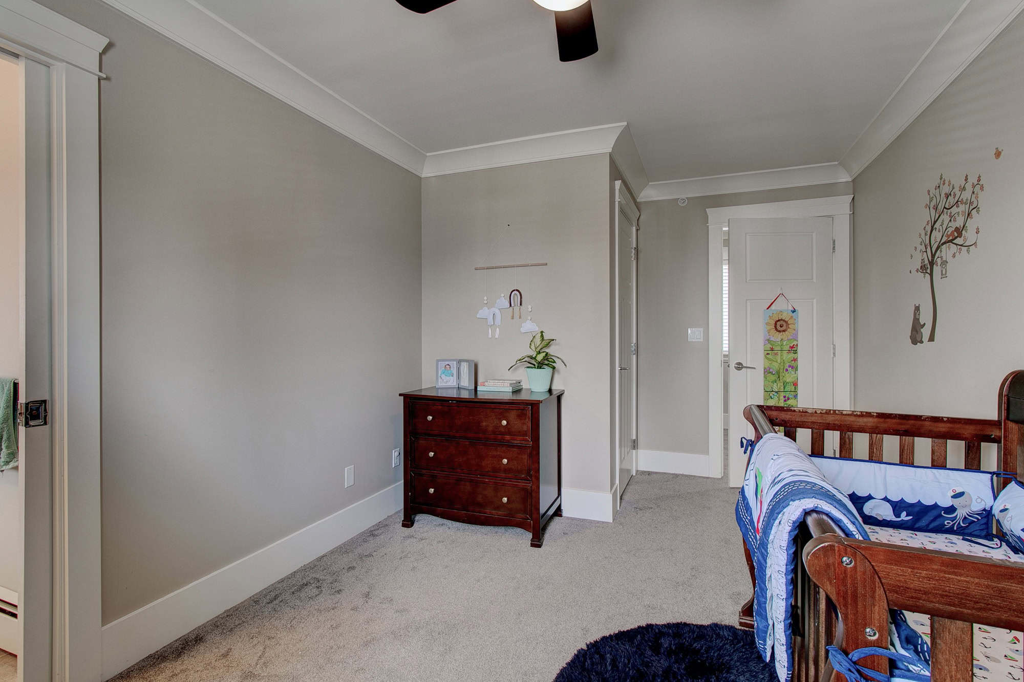 Bright and spacious toddler bedroom with neutral walls and cozy carpet, featuring a wooden crib, colorful child decor, and ample natural light for a comfortable home environment.