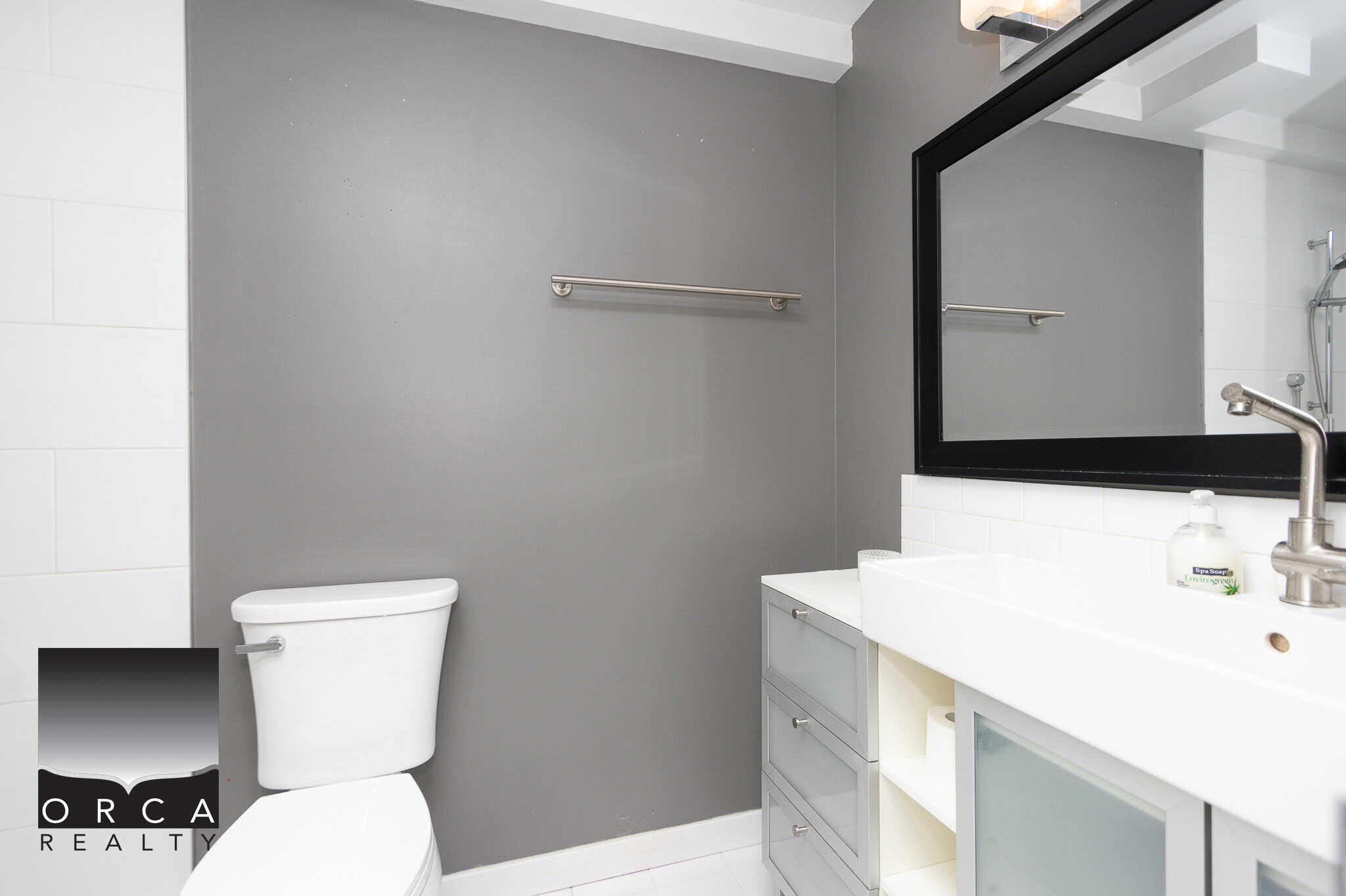 Modern bathroom interior with white toilet, grey wall, and sleek vanity featuring a large mirror, ideal for contemporary homes in Vancouver and surrounding areas.
